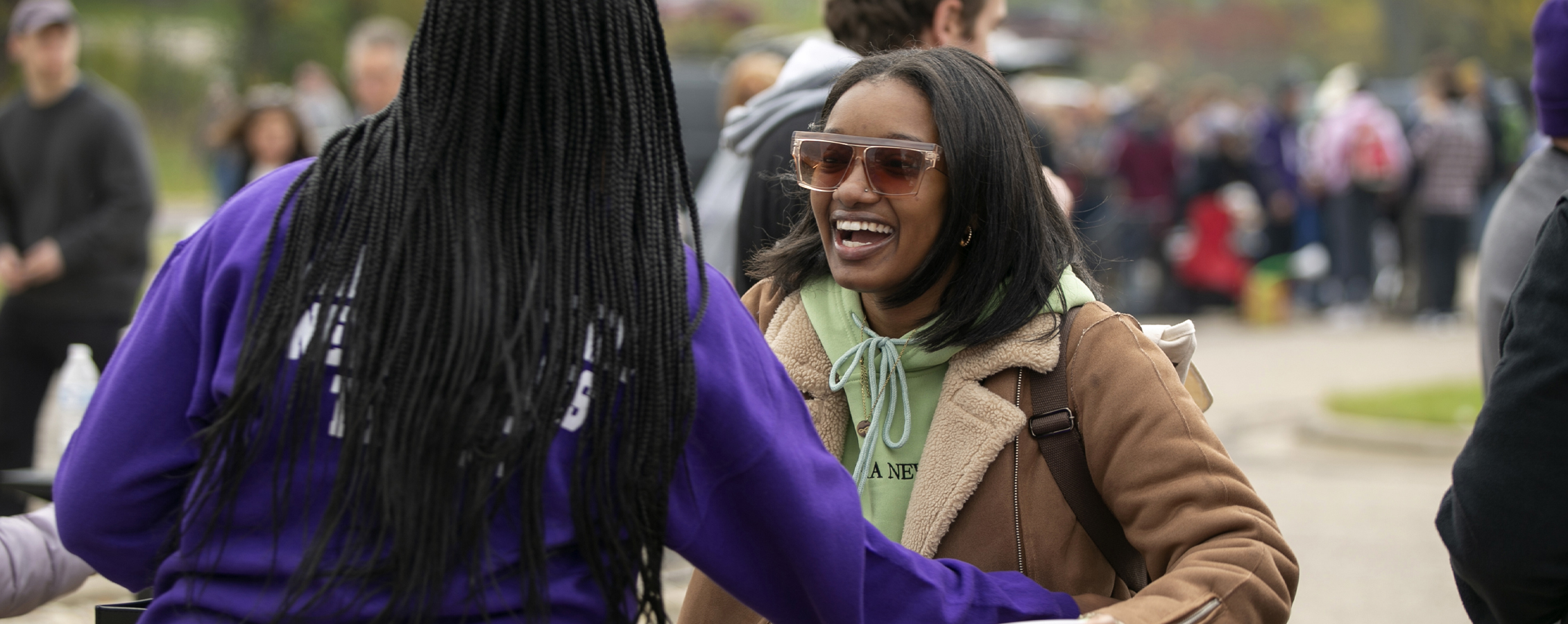 Two students smile and hug outside during a tailgate.