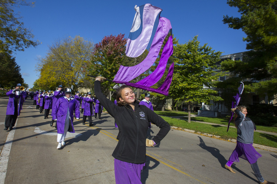 A person wearing purple waves a purple flag in a parade that marches down the street.