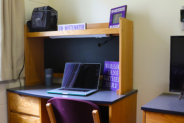 A desk. There is a laptop, a picture and a water bottle on top of the desk.