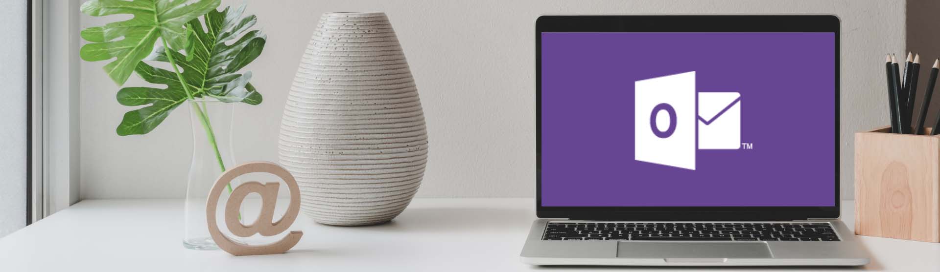 Laptop with a Warhawk purple Outlook logo next to a vase and trendy woodwork