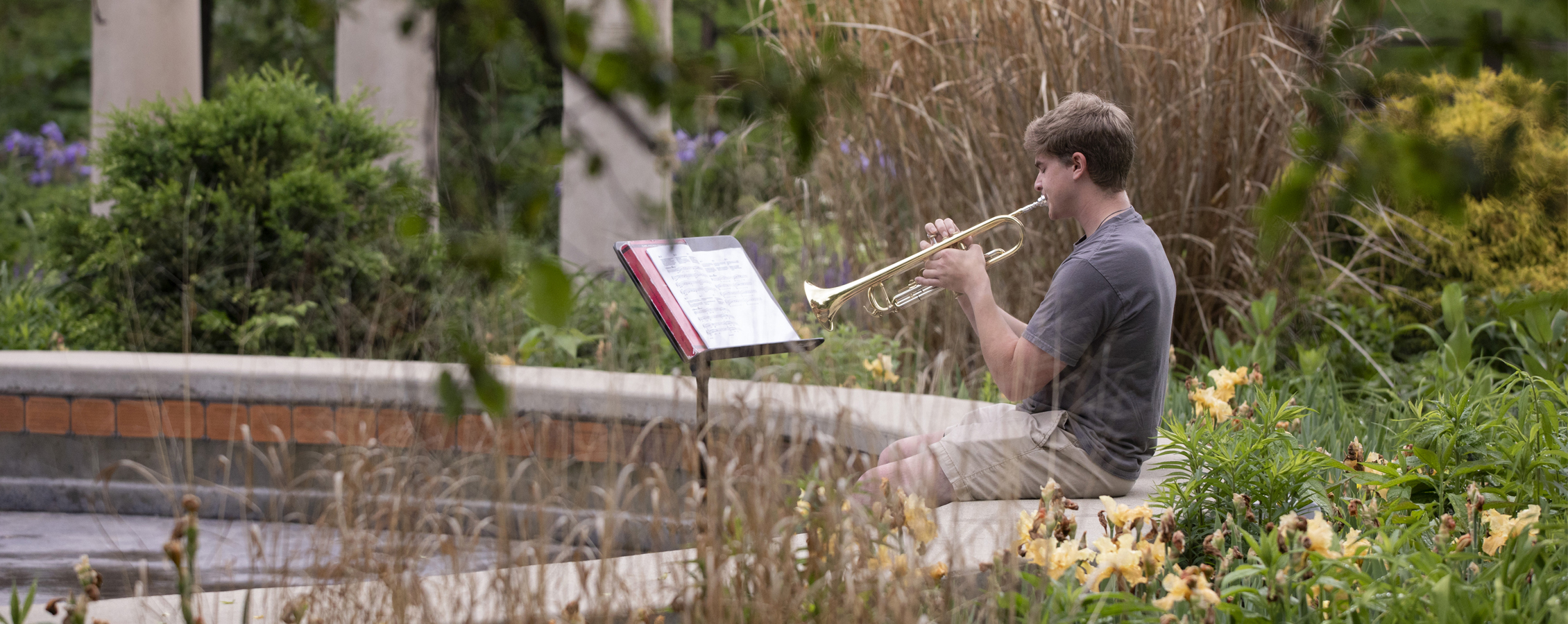 Student playing trumpet in campus garden.