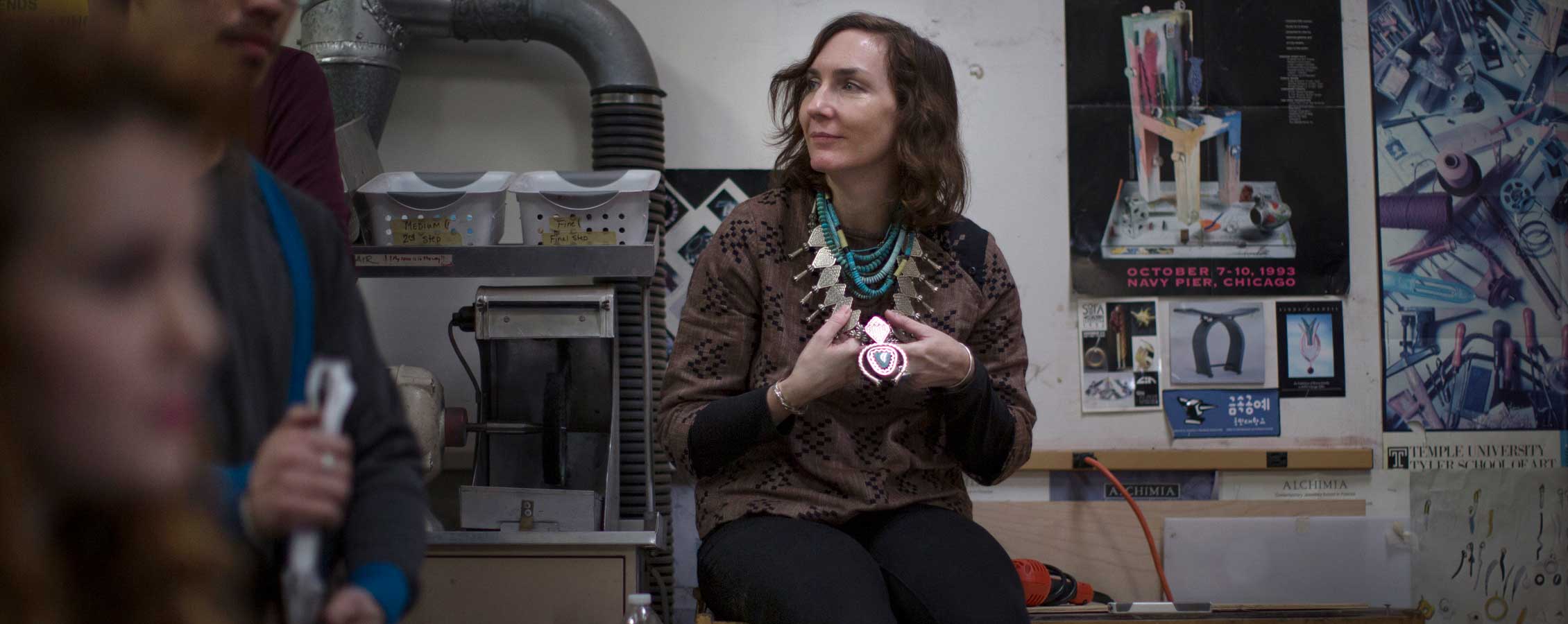 Teresa Faris sits on a table in a jewelry lab.