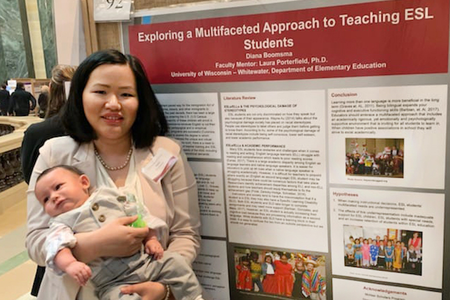 A woman holding a baby stands in front of a research poster.