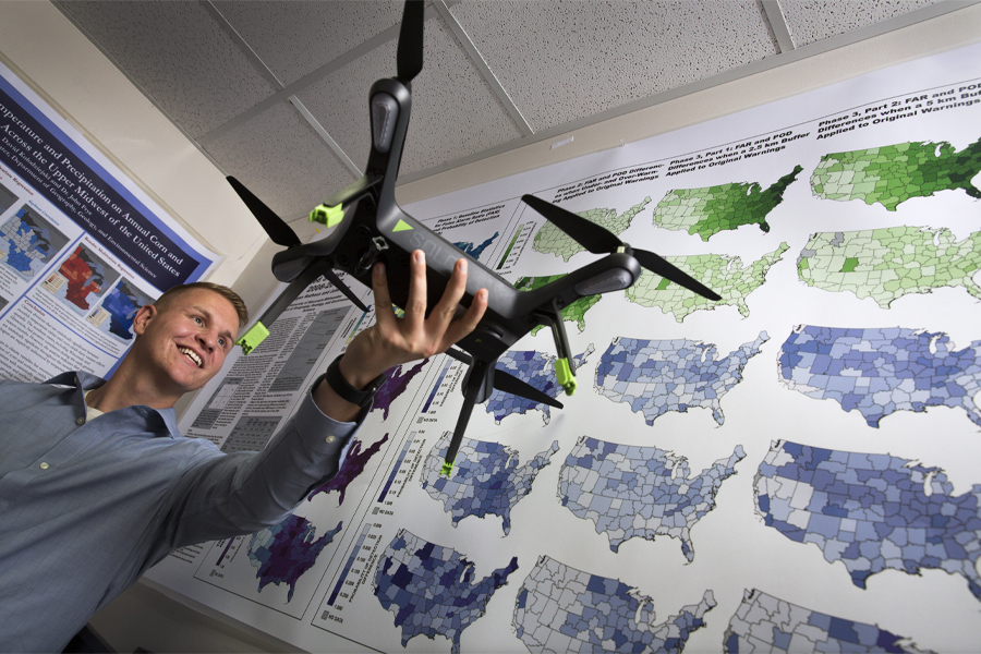 Thor Manson smiles and holds a drone with maps in the background.