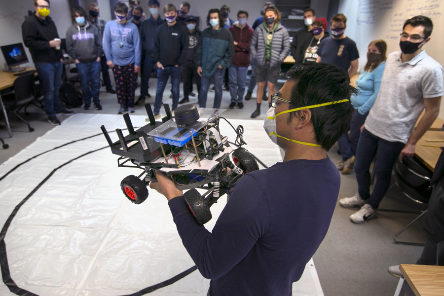 Haijian Sun holds an autonomous vehicle in class with students.