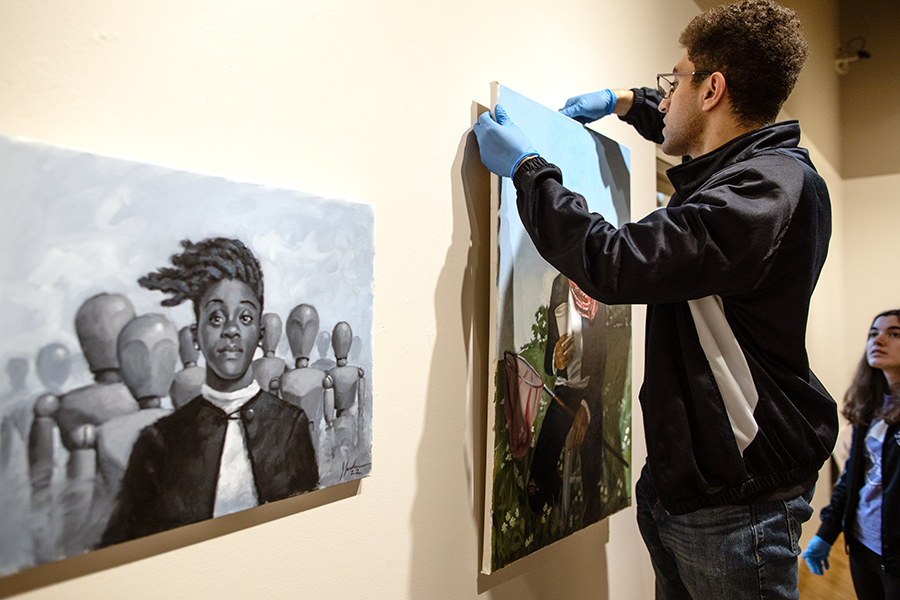 Student hangs art in a gallery with a digital art calculator.