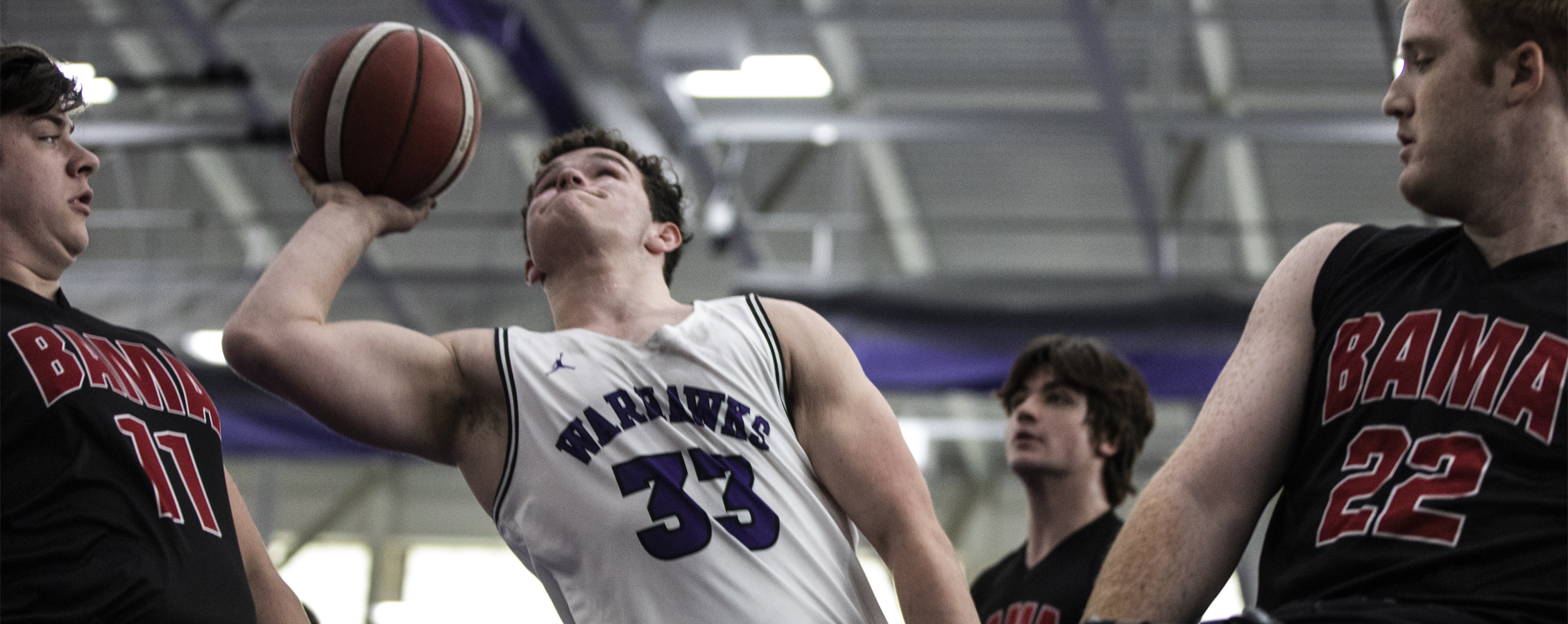 A wheelchair basketball player in a Warhawks uniform shoots the basketball.