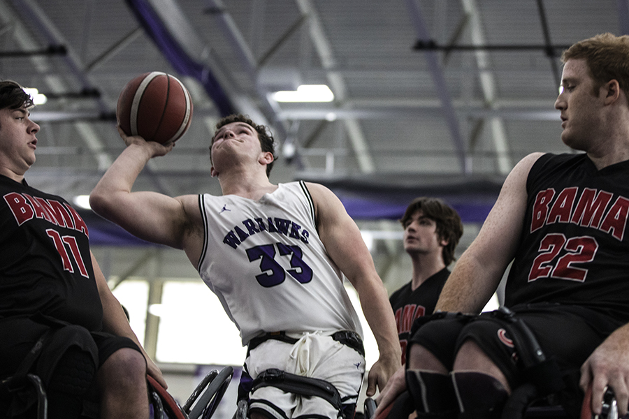 A wheelchair basketball player in a Warhawks uniform shoots the basketball.