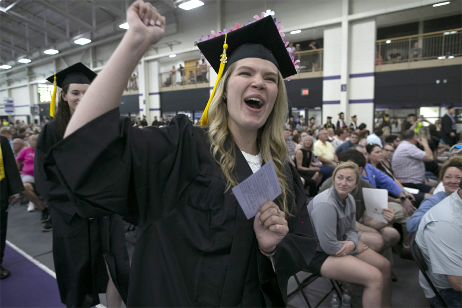 A student wearing her cap and gown cheers in the fieldhouse.