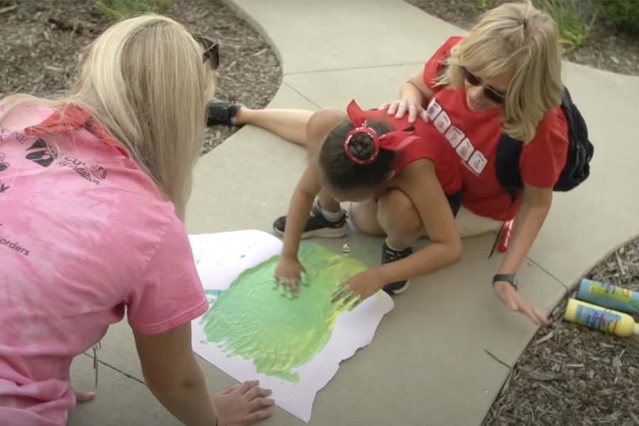 Two adults look on while a child finger paints.