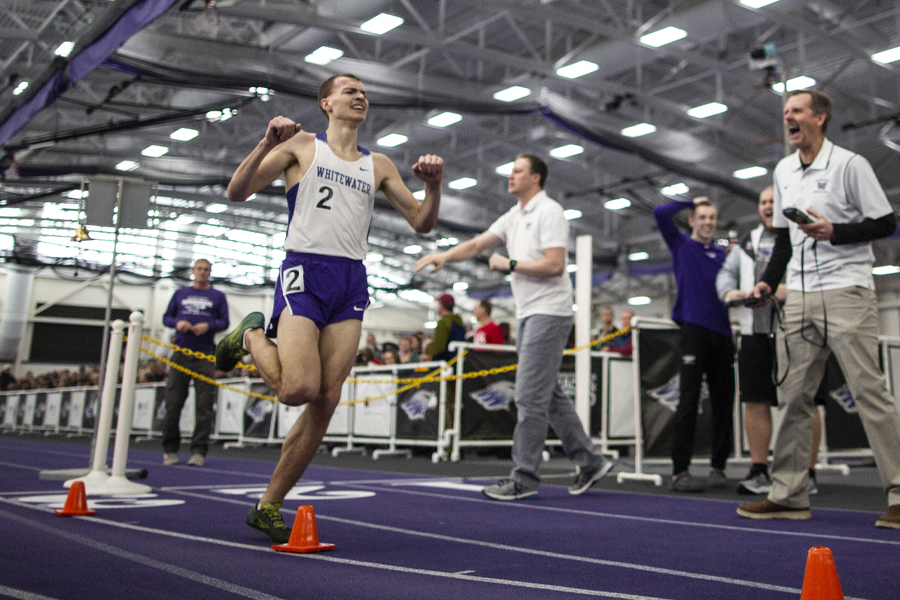 A student athlete crosses the finish line, while his coach yells encouragement from the sideline.