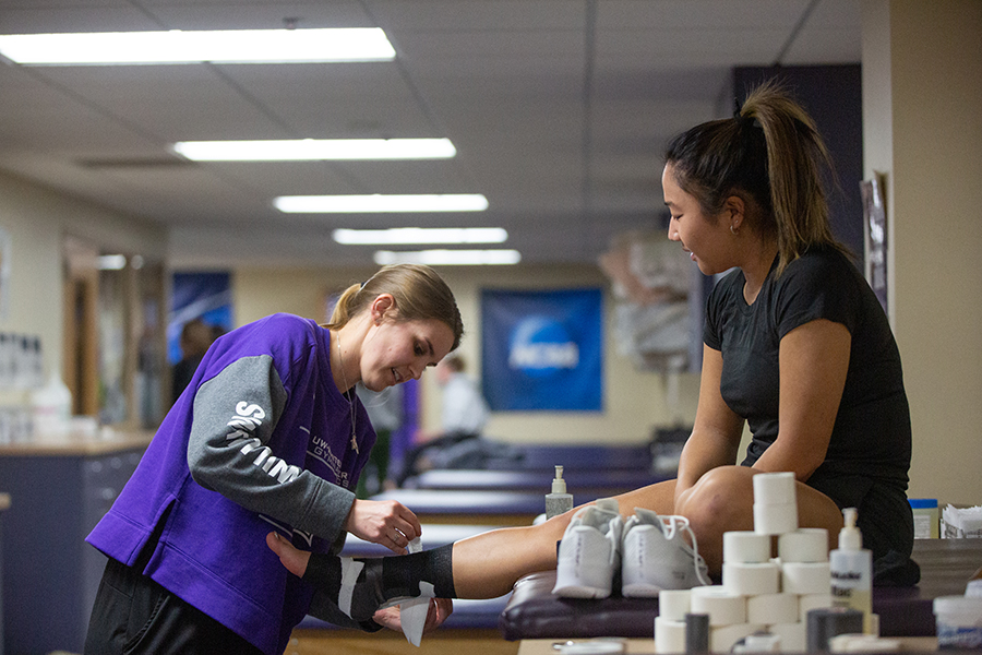 A trainer bandages a Warhawk athlete sitting on a table.