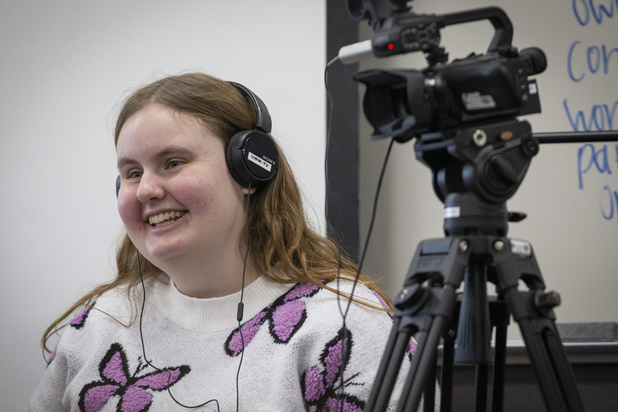 Photo of Angie Carchesi wearing headphones standing next to a video camera.