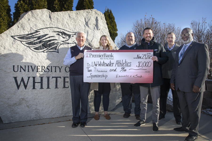 Six people hold a large check and stand by a UW-Whitewater Warhawk monument.