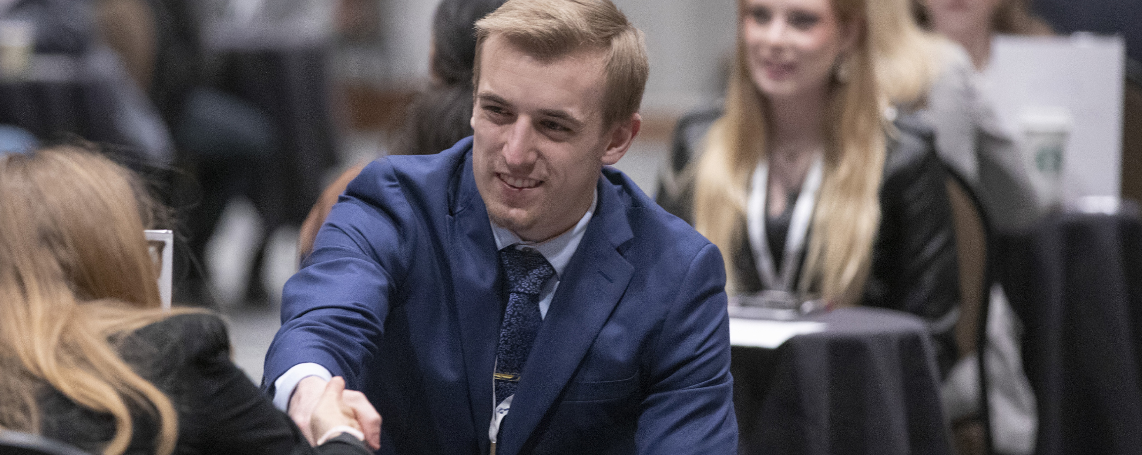 Drew Best, wearing a blue blazer, shakes hands with another person.