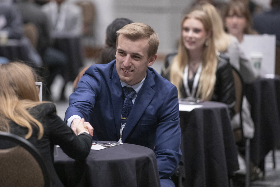 Drew Best, wearing a blue blazer, shakes hands with another person.