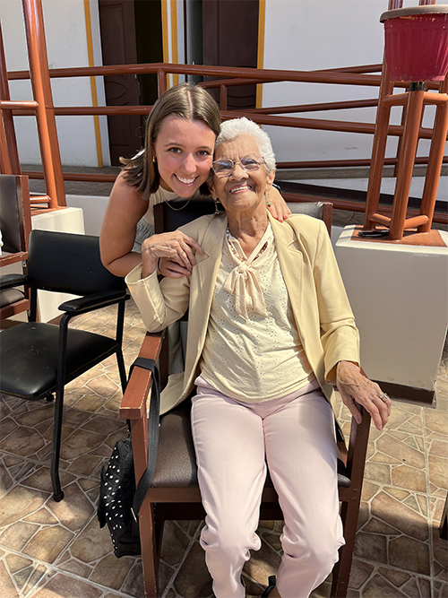 A student hugs an eldery person who is sitting in a chair.