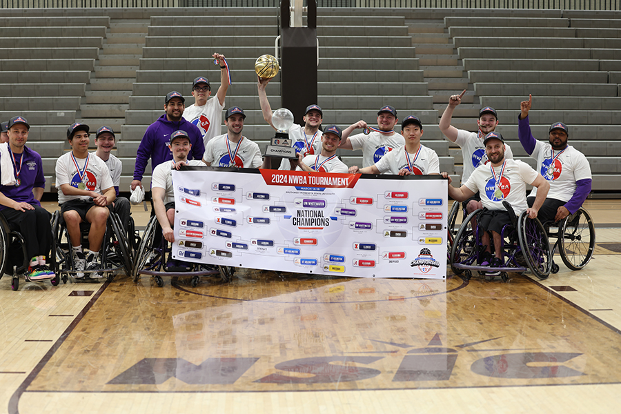 The wheelchair basketball team gathers together and holds a national champions banner.