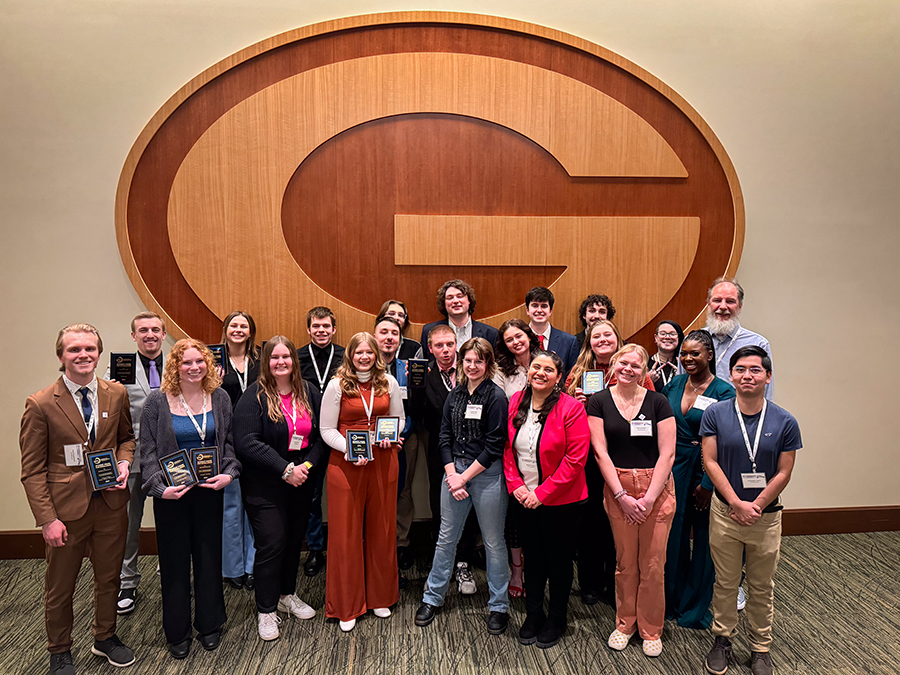 A group of people pose together in front of a wood-carved G for the Green Bay Packers.