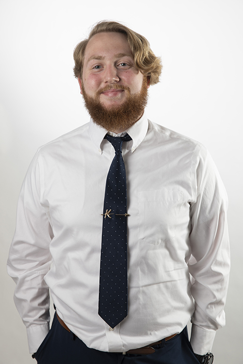 Kolden, wearing a shirt and tie, smiles at the camera with his hands in his pockets.