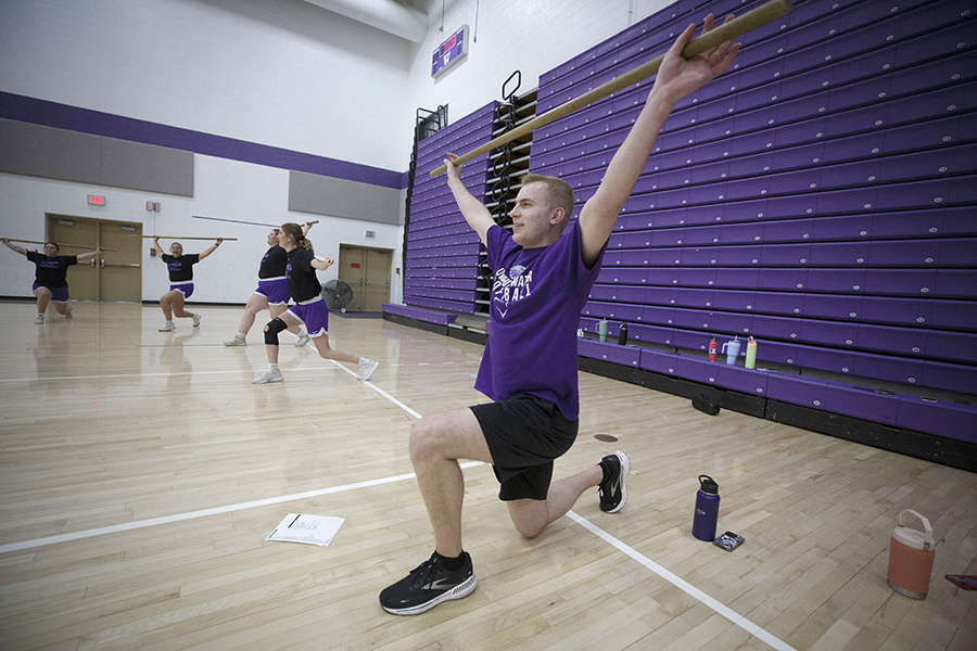 Ty Jahnke kneels on a gym floor with a bar above his head to demonstrate a stretch.