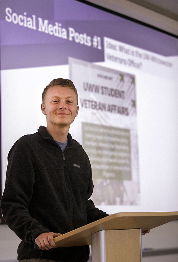 Dylan Riley stands behind a podium and smiles at the camera.