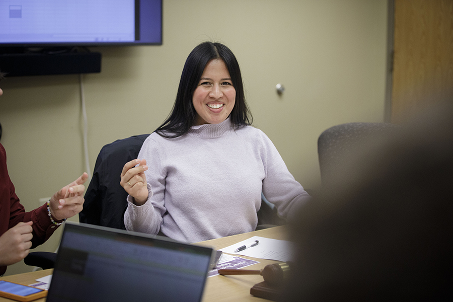 Maria pacheco smiles while sitting around a table with other people.