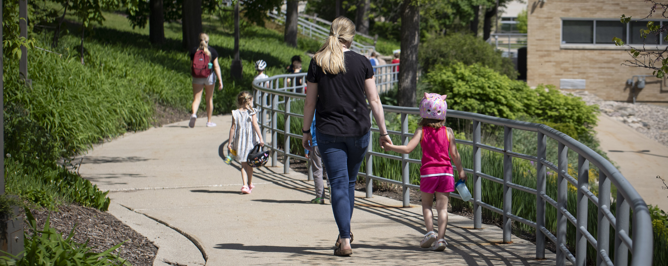 A teacher from the Children's Center holds hands with a child as they walk down a path on campus.