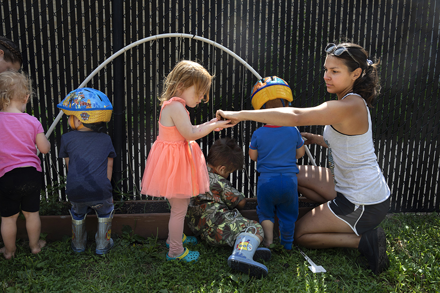 A UW-Whitewater student kneels with five small children and hands seeds to a little girl.