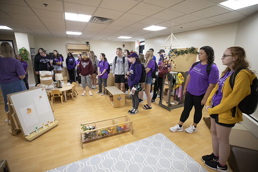 A group of students, mostly wearing purple shirts, gather in a Children's Center classroom.