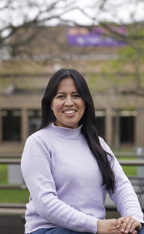 Maria Pacheco stands in front of a colorful mural and smiles at the camera.