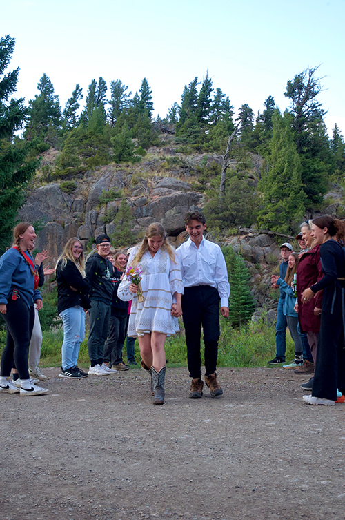 The married couple walks through a small crowd of people with mountains in the background.