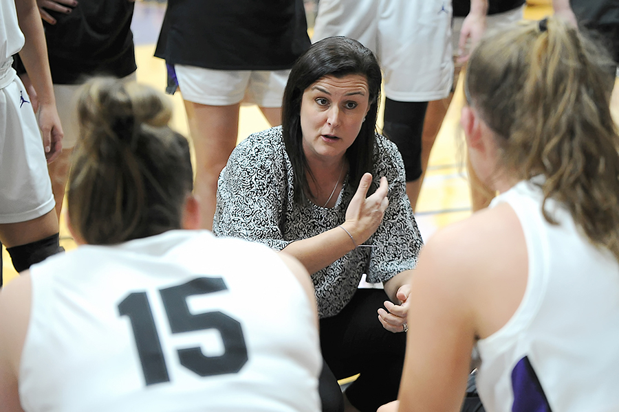 Keri Carollo kneels down to speak to two female basketball players.