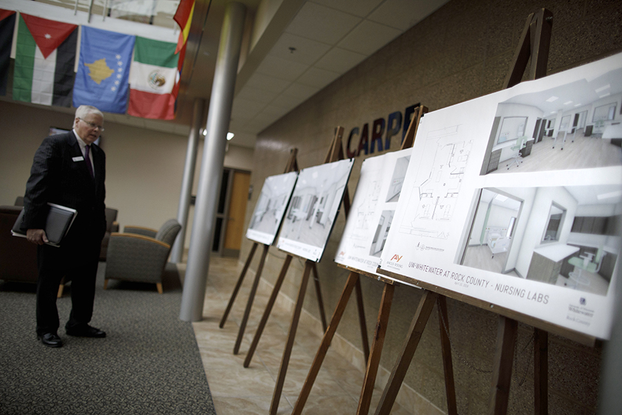 A man stands in an open room and looks at project drawings and floor layouts of the new nursing lab.