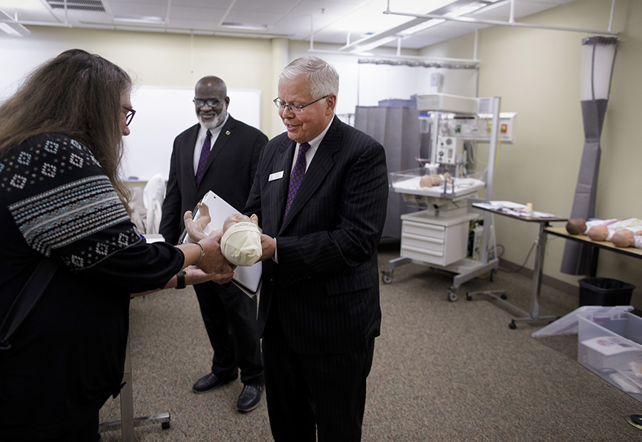 A man holds a newborn simulator doll in a classroom. 