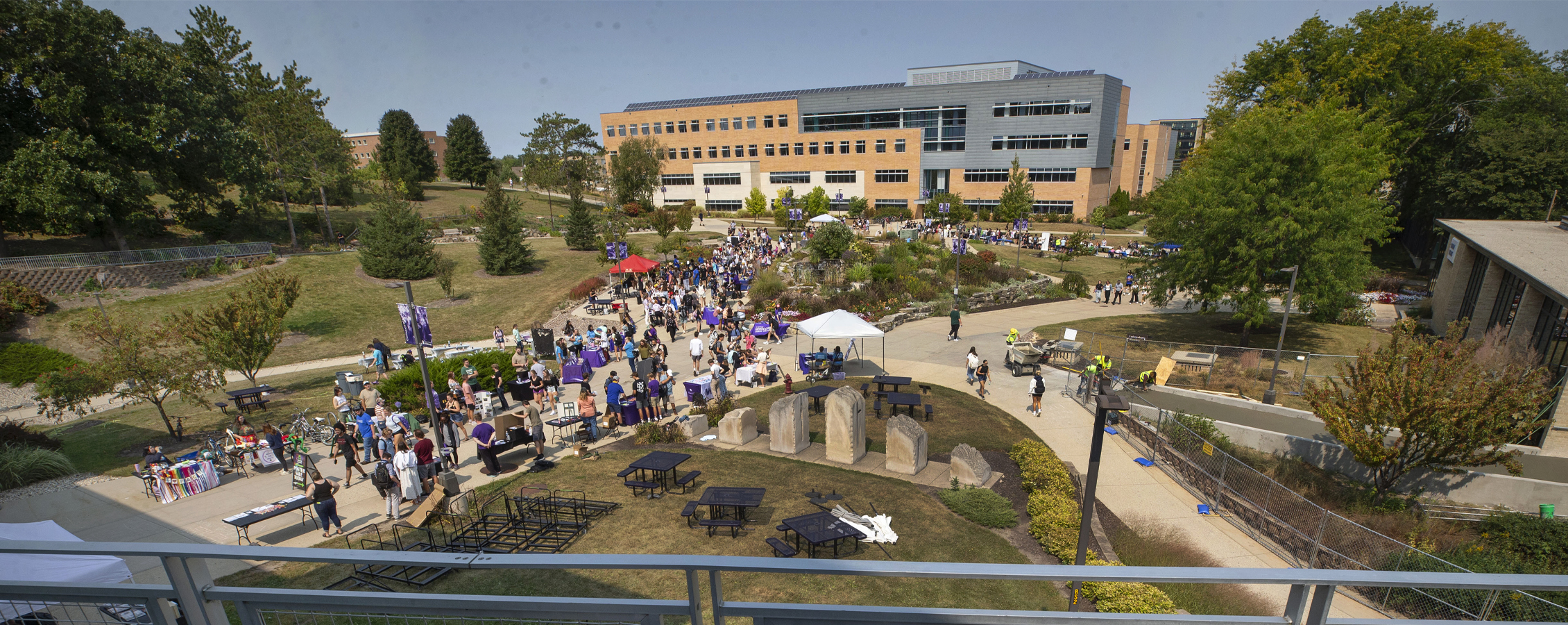 Students fill the sidewalks in the middle of campus with Hyland Hall in the background.