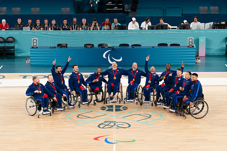 The men's Team USA gathers on the basketball court wearing gold medals.