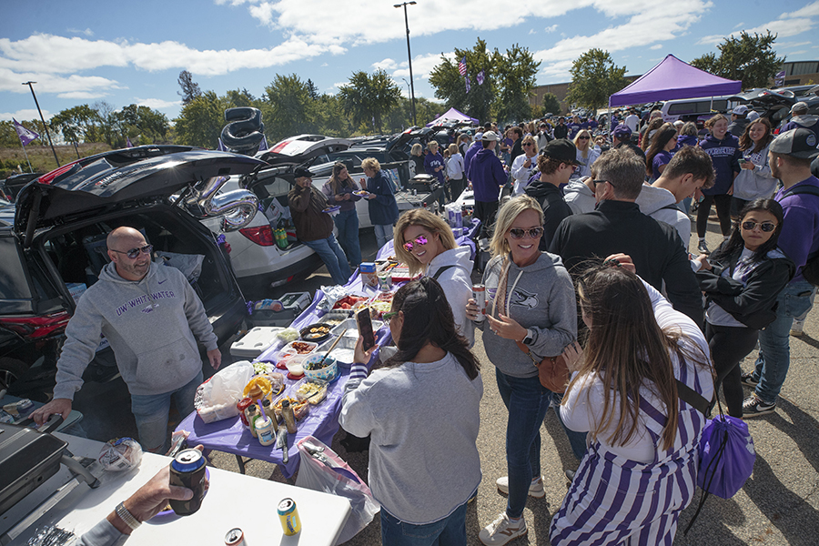 The parking lot is full of vehicles and people wearing various colors of purple as they tailgate.