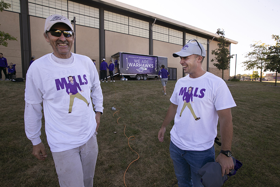 Coach Jeff Miller, wearing a shirt that says Mills, laughs with another person. 