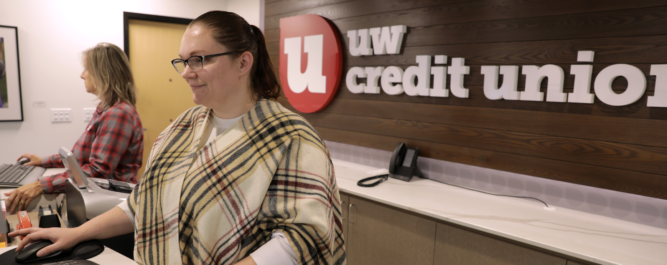 A person works at a computer with the UW Credit Union sign behind them.