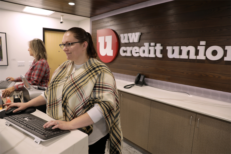 A person works at a computer with the UW Credit Union sign behind them.