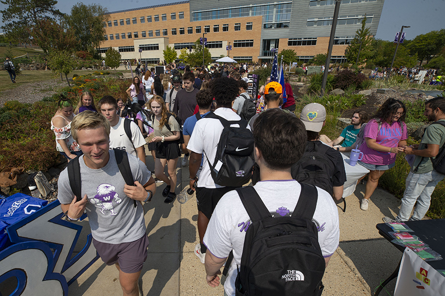 Students fill the sidewalks in the middle of campus with Hyland Hall in the background.