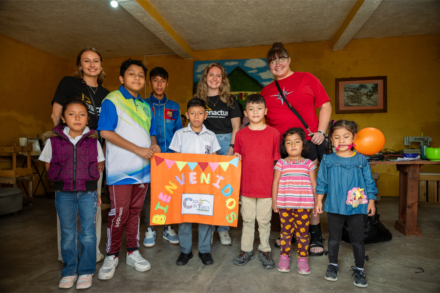 Three students stand with a group of Guatemala children who hold a colorful banner.