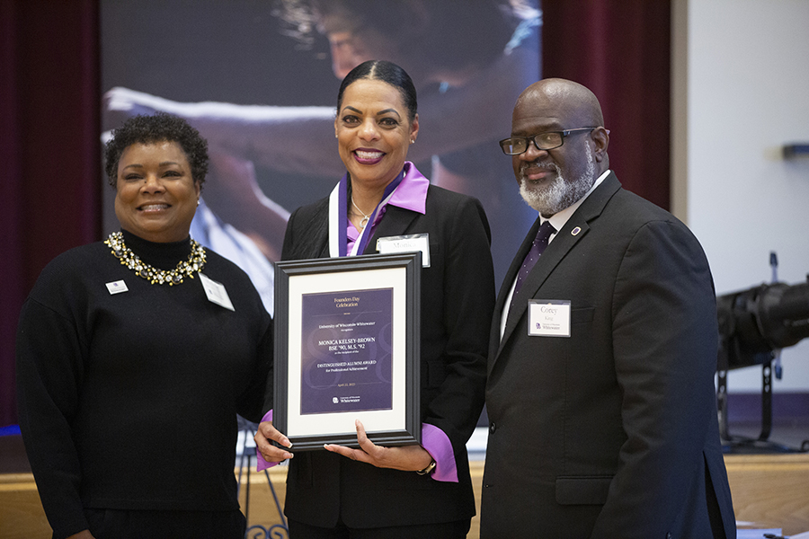 Monica Kelsey-Brown stands with Michelle Buckingham and Chancellor King while she holds a plaque.