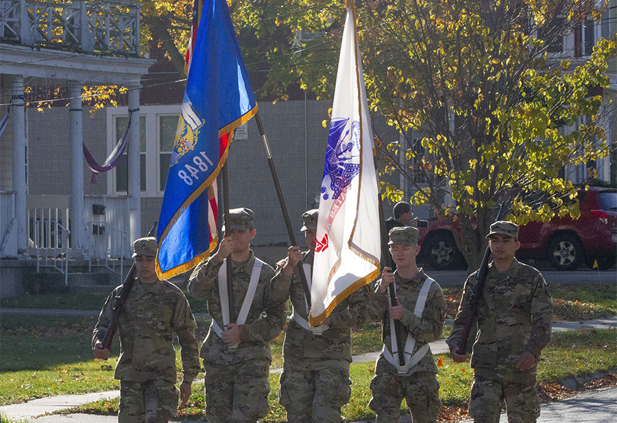 An ROTC Color Guard carries flags as they march down the street.