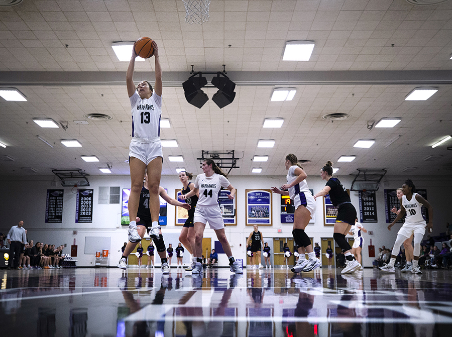 A member of the basketball team seems to jump straight in the air toward the basket with the ball in her hands.