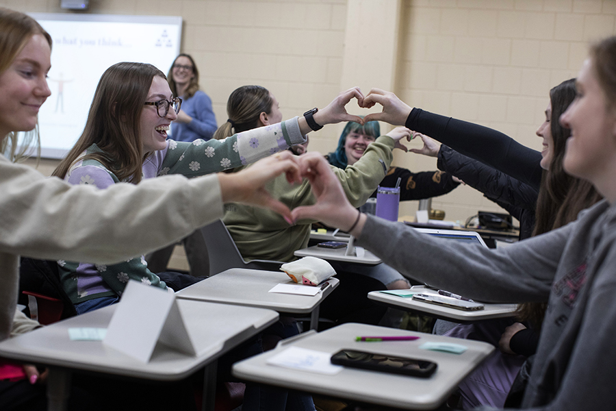 Students sit across form each other and connect their hands to make a heart.