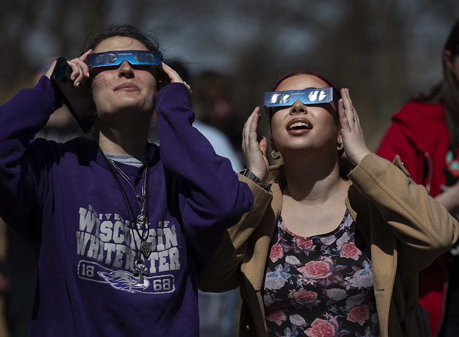 Two students hold solar eclipse glasses to their faces as they look up into the skit.