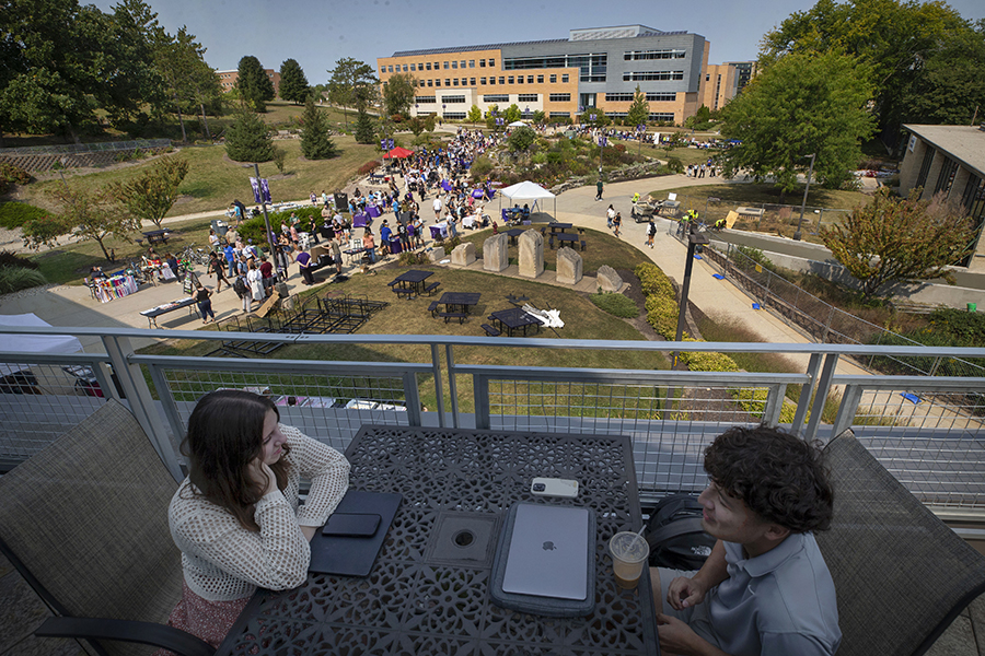 Students fill the sidewalks in the middle of campus with Hyland Hall in the background.