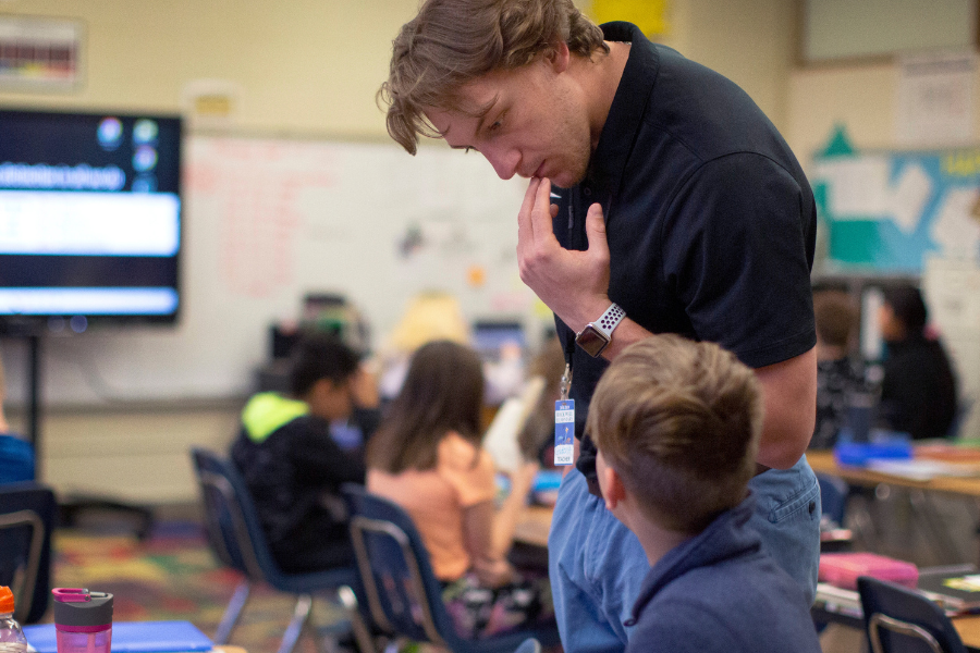 Student standing next to a child in a classroom.